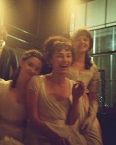 three women in white dresses sitting next to each other and one woman is smiling at the camera