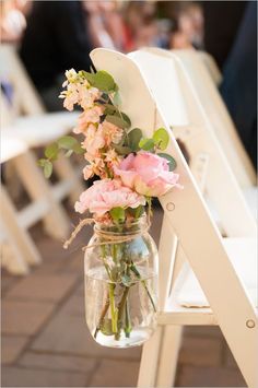 flowers in a mason jar sitting on a white chair at an outdoor wedding ceremony,