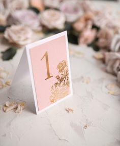 the table numbers are placed on top of each other with flowers in the background and petals scattered around them