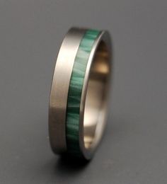 a wedding ring with green wood inlays on the inside and silver band, sitting on a gray surface