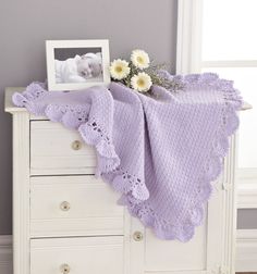 a baby blanket with flowers on top of it next to a dresser and photo frame