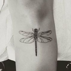 a black and white photo of a dragonfly tattoo on the right arm, with an insect in it's center