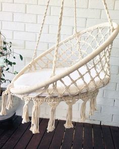 a white hanging chair with tassels on the bottom, and a potted plant next to it