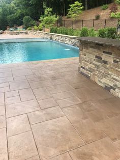 an outdoor swimming pool surrounded by stone walls and landscaping features, including a fire pit