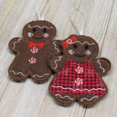 two brown gingerbread cookies with red and white checkered dresses hanging from strings on wooden surface