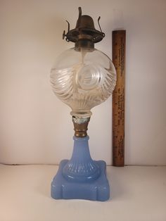 an old fashioned glass lamp on a blue base with a ruler in the back ground