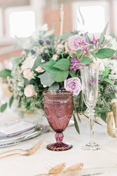 the table is set with wine glasses, silverware and floral centerpieces on it