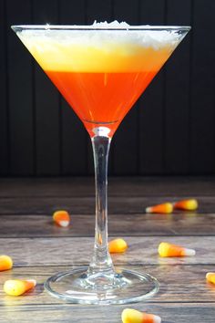 an orange and white drink in a martini glass with candy corn on the table next to it