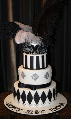 a three tiered cake decorated with black and white stripes, feathers, and mardi gras decorations