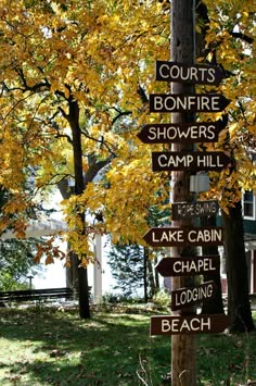 a pole with many signs on it in front of a house and trees that have yellow leaves