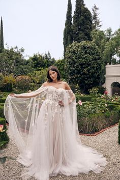 a woman in a white wedding dress posing for the camera with her veil flowing over her shoulder