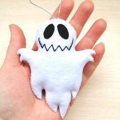 a hand is holding a white ornament with black eyes and a ghost face