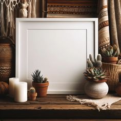 a white frame sitting on top of a wooden table next to potted plants and candles