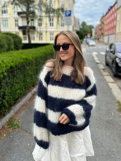 a woman is standing in the street wearing a striped sweater and white dress with black sunglasses