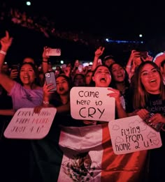 a group of people holding up signs in the air at a concert with their cell phones