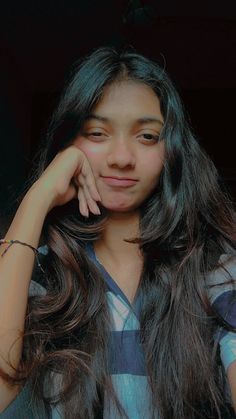 a woman with long dark hair posing for a photo while holding her hand on her chin