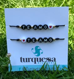 two beaded bracelets sitting on top of a sign in the grass with words teamo, teamo and turquesa