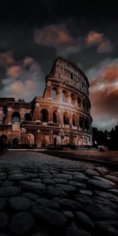 the colossion in rome at night with dramatic clouds above it and cobblestones on the ground