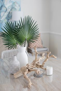 a table topped with white vases filled with palm leaves next to candles and a candle holder