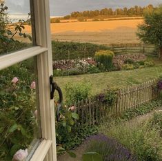 an open window looking out onto a field with flowers and trees in the foreground