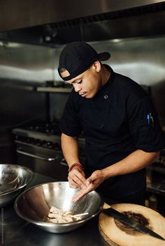 a man in a black shirt and hat is cooking food on a silver pan with wooden spoons