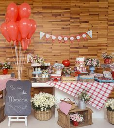 a table topped with lots of red balloons next to a chalkboard sign and baskets filled with flowers