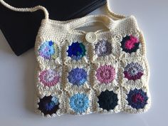 a crocheted granny bag sitting on top of a white table next to a black purse