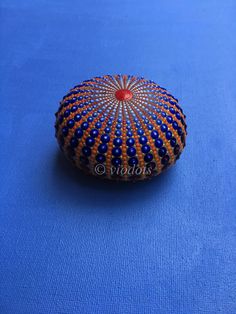 an orange and blue beaded round box on a blue surface with a red center