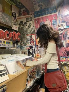 a woman standing in front of a counter with records on the wall and posters behind her