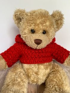 a teddy bear wearing a red sweater sitting on top of a wooden floor in front of a white wall