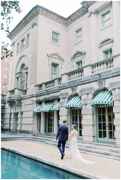 a bride and groom walking in front of a large building with a pool on the side