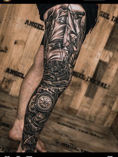 a man's leg with a ship and compass tattoo on it, in front of a wooden wall