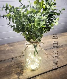 a vase filled with green plants sitting on top of a wooden table