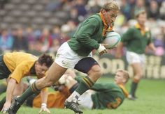 a rugby player runs with the ball in his hands as other players watch from the sidelines