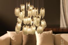 a chandelier hanging from the ceiling in a living room with pillows and throw pillows