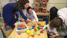 two women and a child sitting at a table in a playroom with toys on it