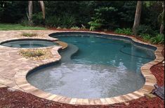 a small pool surrounded by landscaping in the middle of a yard with brick edging around it