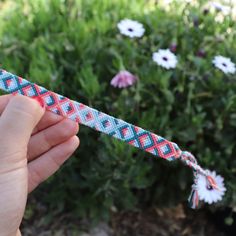 a hand holding a string with flowers in the background