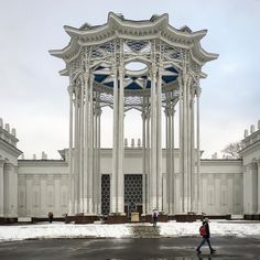 a person walking in front of a white building with columns and arches on the sides