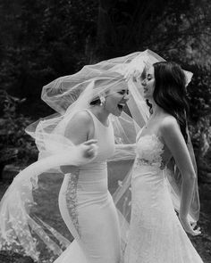 two women in wedding gowns are laughing at each other while one holds her veil over her head