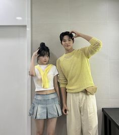 a man and woman standing next to each other in front of a white tiled wall