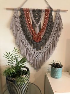 there is a plant in a pot on the table next to a wall hanging with tassels