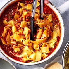 a person holding a ladle in a bowl full of pasta and sauce with cheese on the side