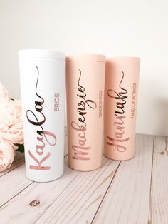 three pink and white coffee mugs sitting on top of a wooden table next to flowers