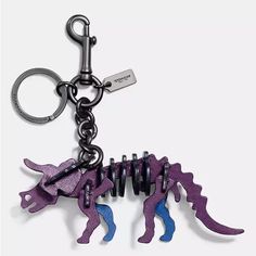 a purple dinosaur keychain hanging from a black metal hook on a white background