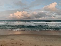 there is a beach with waves coming in to the shore and clouds above it on a cloudy day