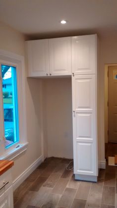 a kitchen with white cabinets and tile flooring next to a window in the corner