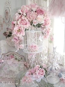 a white birdcage filled with pink flowers on top of a table