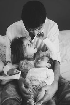 a man holding two small children in his arms while they are sitting on a bed