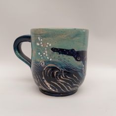 a ceramic mug with a whale on it's side and waves in the water